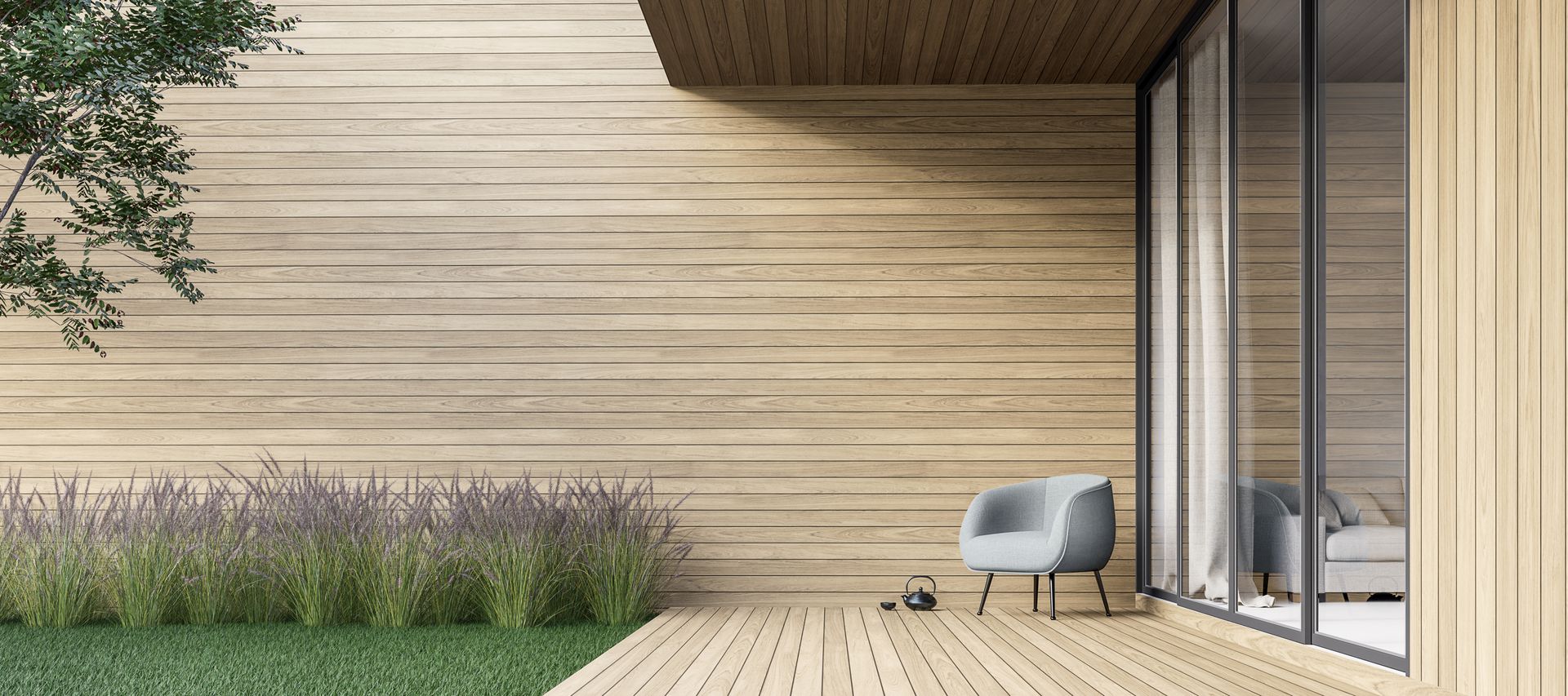 Helle Terrassendielen vor einer Holzfassade mit Glasfront, Rasenfläche und Ziergräsern