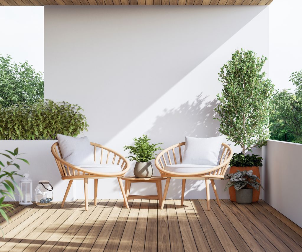 Zwei Holzsessel mit Kissen und Beistelltisch auf einer kleinen Terrasse mit Pflanzen und Holzdeck.