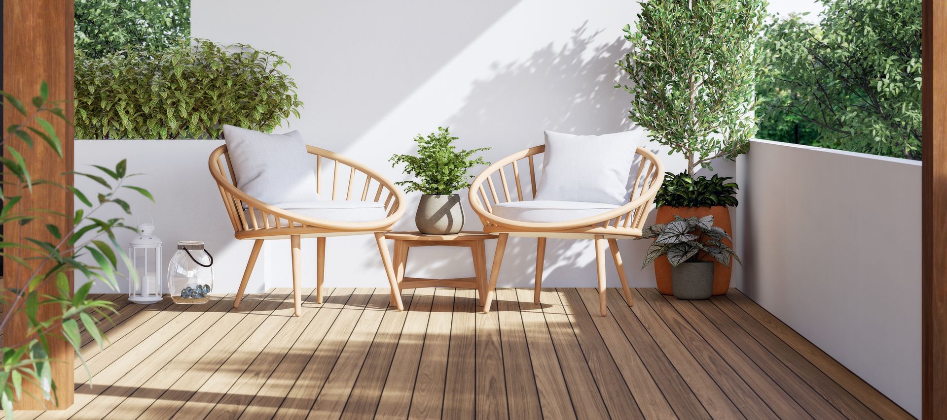 Zwei Holzsessel mit Kissen und Beistelltisch auf einer kleinen Terrasse mit Pflanzen und Holzdeck.