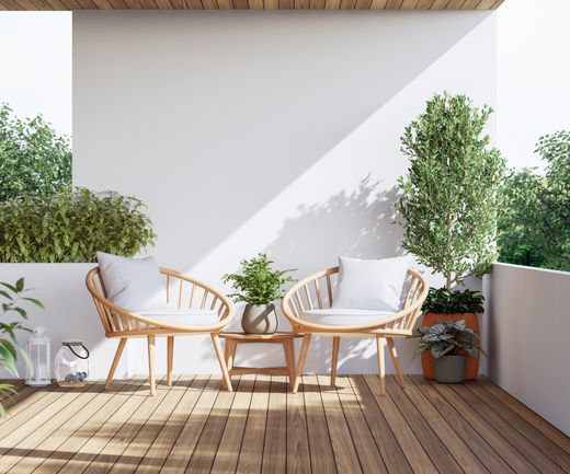 Zwei Holzsessel mit Kissen und Beistelltisch auf einer kleinen Terrasse mit Pflanzen und Holzdeck.
