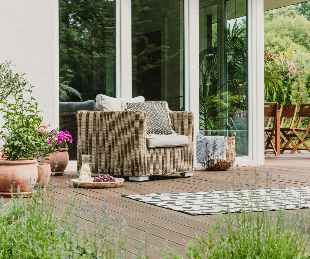 Terrasse mit Rattansessel, Pflanzkübeln und Sitzbereich vor einer modernen Glasfront