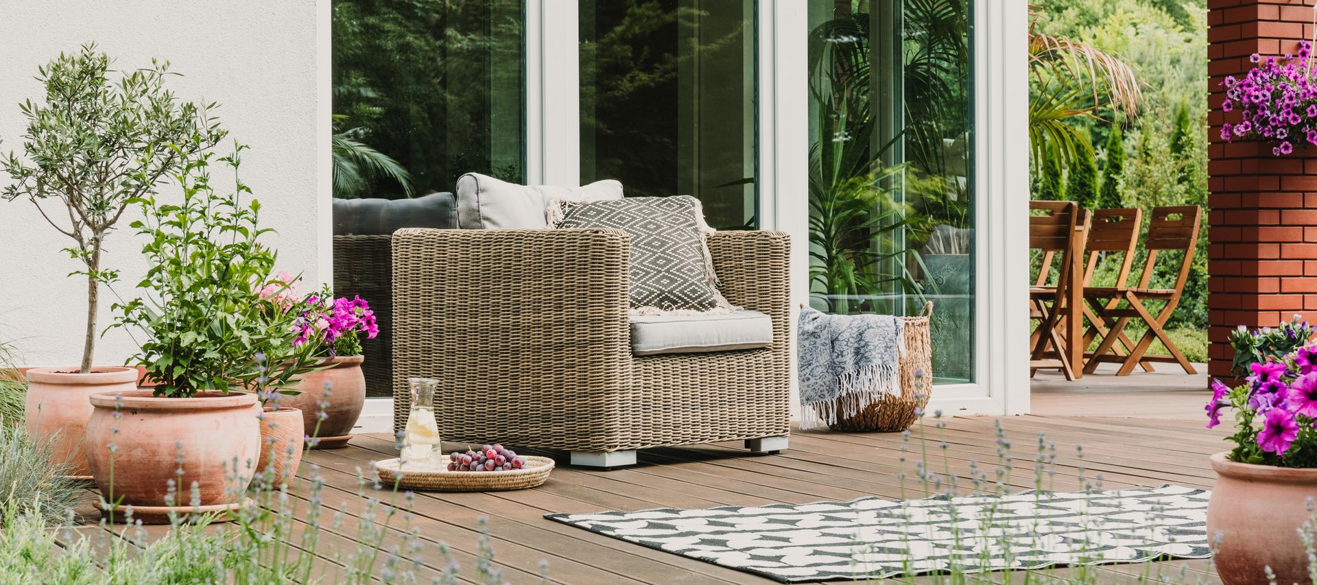 Terrasse mit Rattansessel, Pflanzkübeln und Sitzbereich vor einer modernen Glasfront