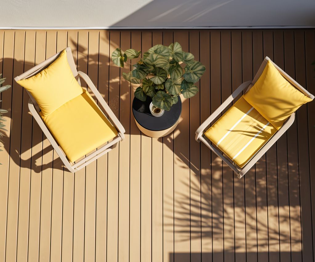 Zwei Gartenstühle mit gelben Polstern auf einer modernen Terrasse aus Holz oder WPC, Draufsicht mit Pflanze in der Mitte