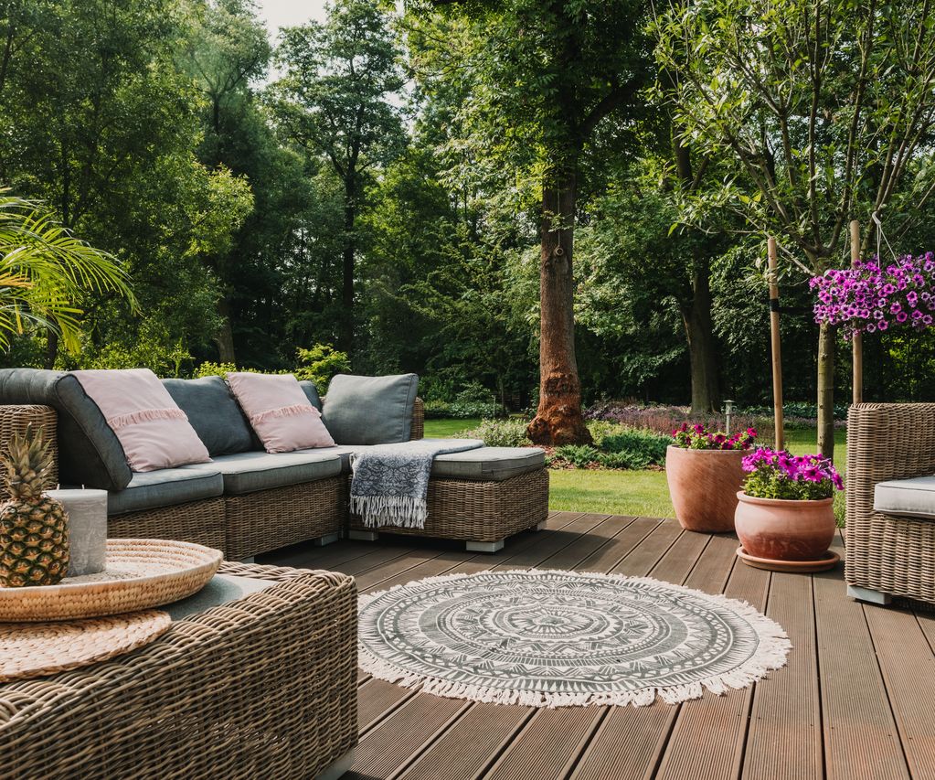 Terrasse mit braunen Terrassendielen, Rattan-Sitzgruppe und Pflanzkübeln in einem begrünten Garten