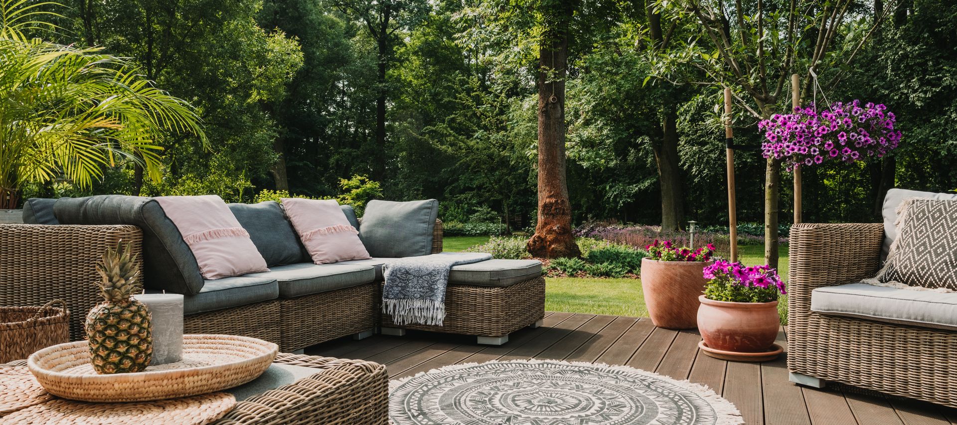 Terrasse mit braunen Terrassendielen, Rattan-Sitzgruppe und Pflanzkübeln in einem begrünten Garten