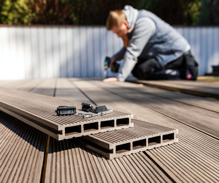 Handwerker montiert WPC-Terrassendielen mit Schrauben und Clips auf einer Unterkonstruktion im Garten