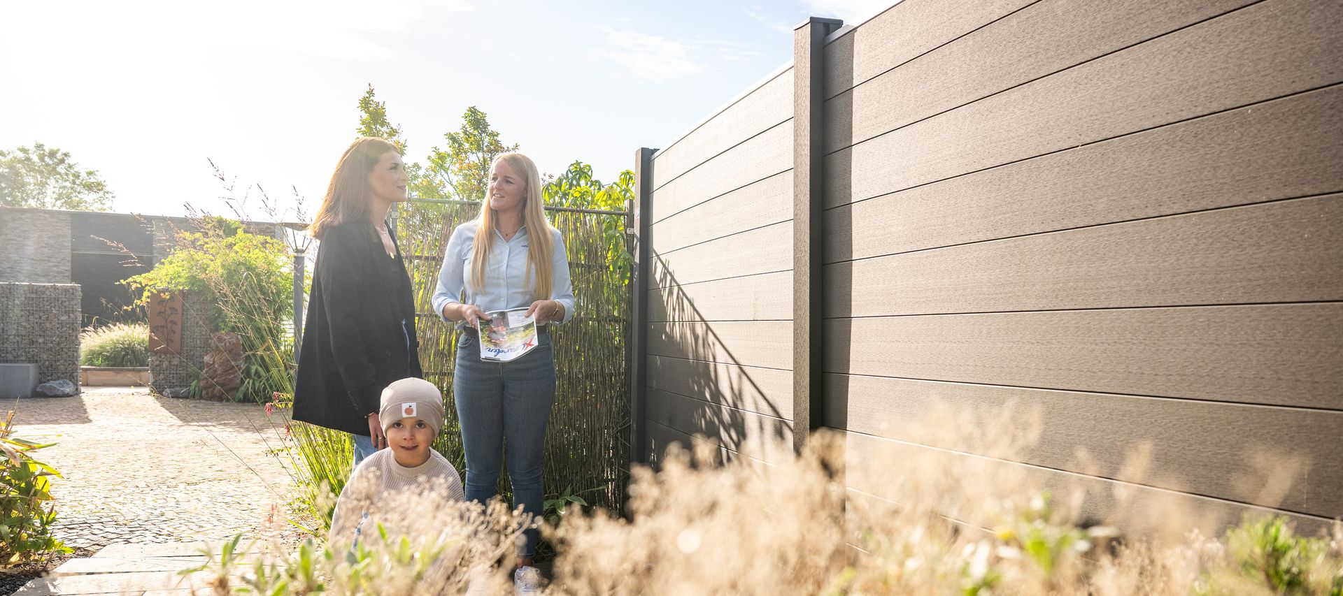 Kundin mit Sohn wird in Gartenausstellung von Fachberaterin zu Zäunen beraten, bauXpert Gr Beilage Vechta Holz Baustoffhandel Garten- und Landschaftsbau