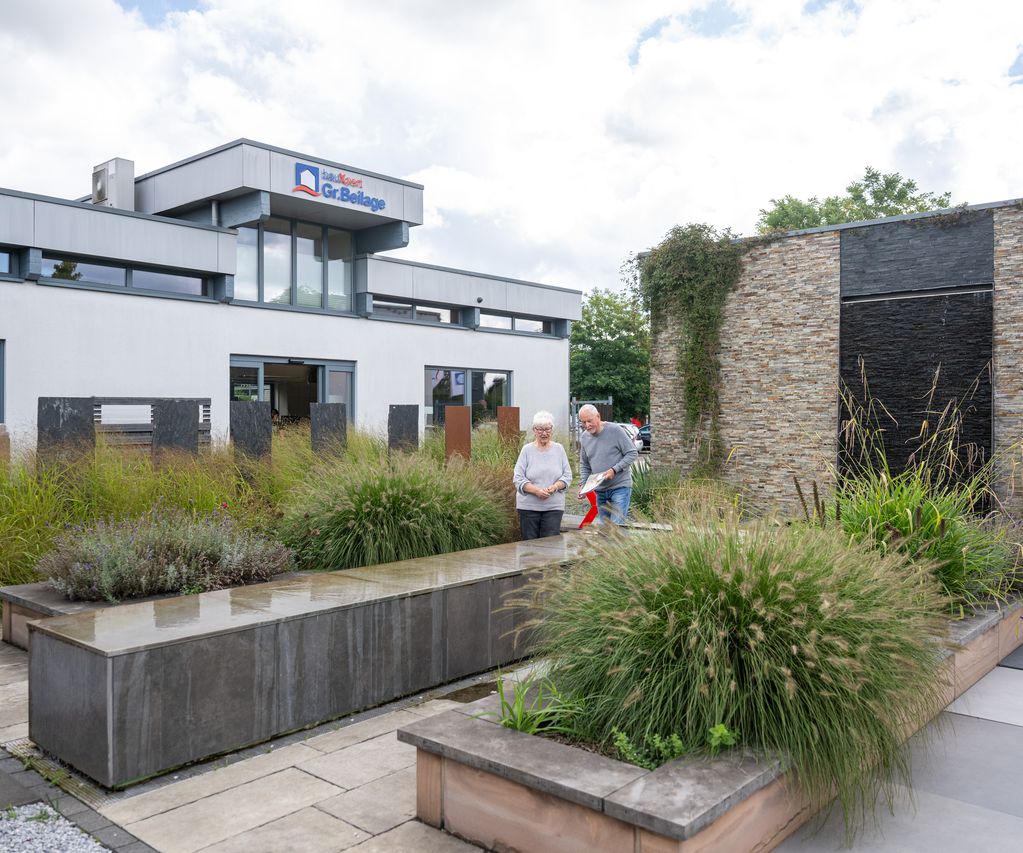 Kundenpaar läuft durch die bauXpert Ausstellung mit Garten- und Pflasterflächen