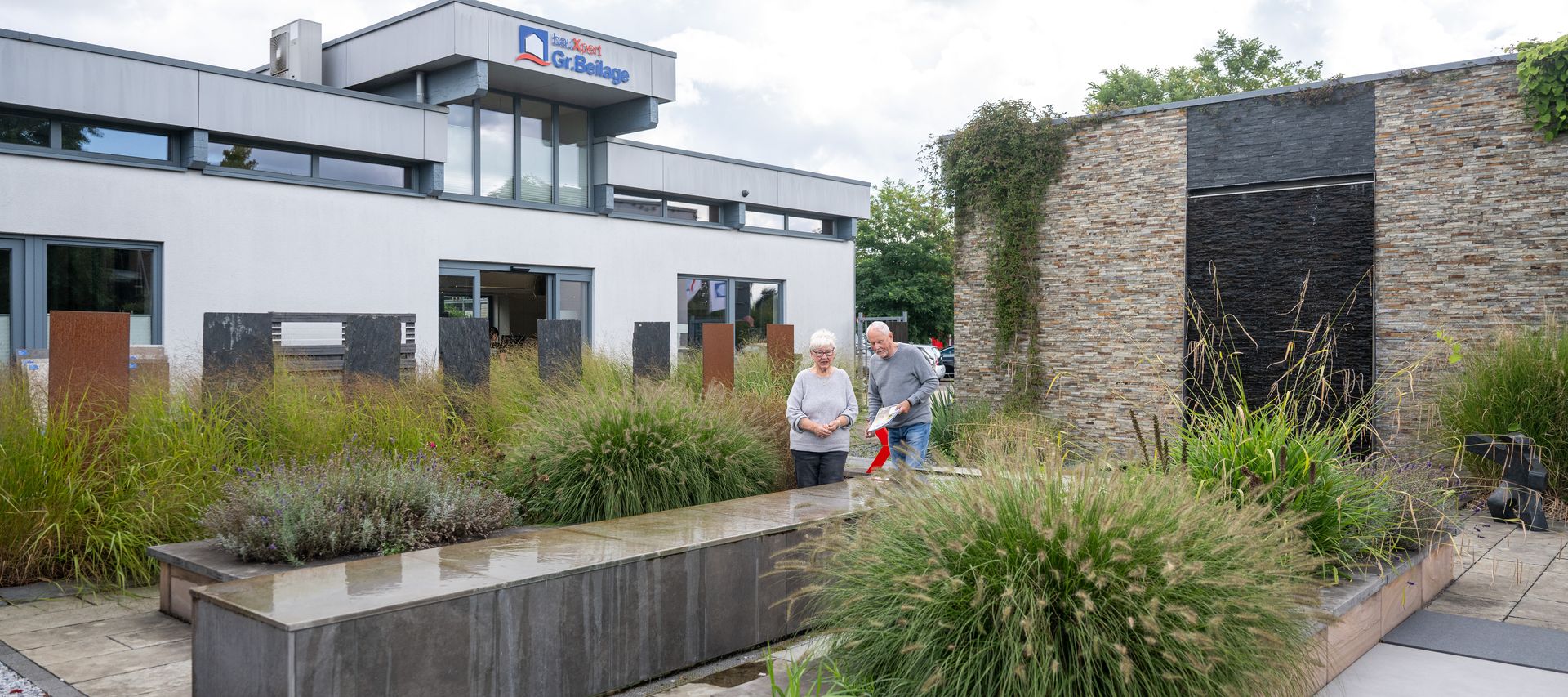 Kundenpaar läuft durch die bauXpert Ausstellung mit Garten- und Pflasterflächen