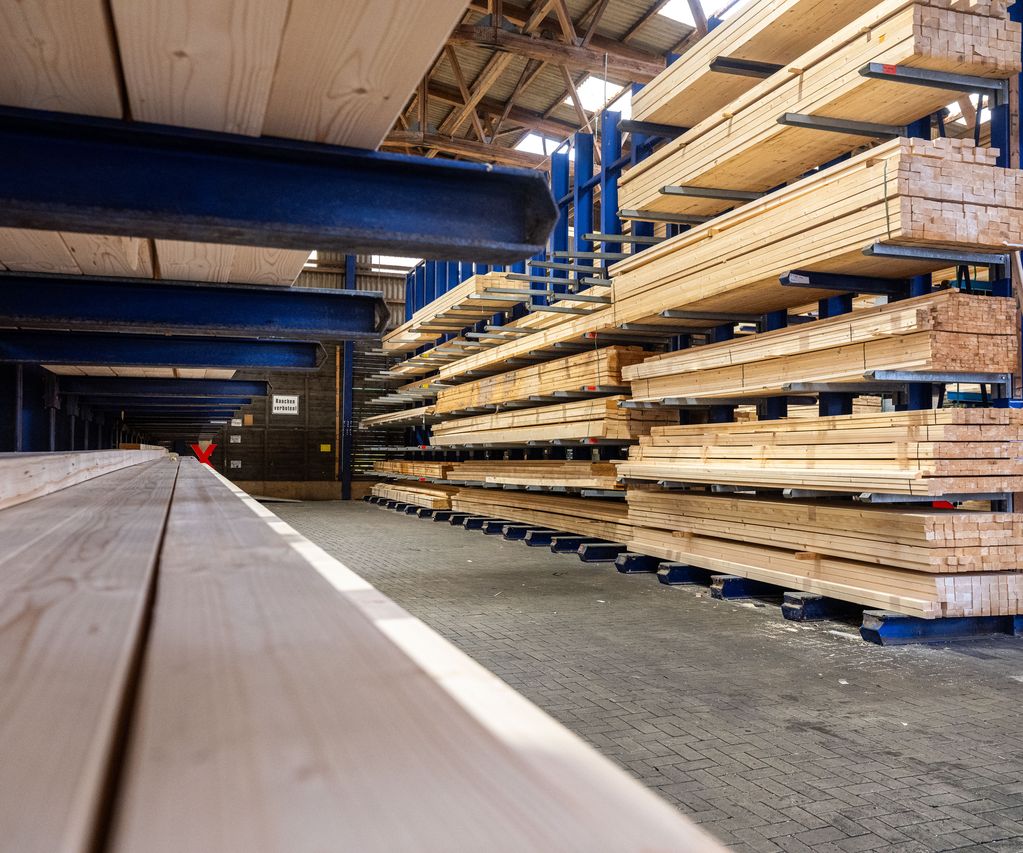 Holzlager von bauXpert Gr. Beilage mit langen Holzbalken in Regalen und Transportwagen im Gang