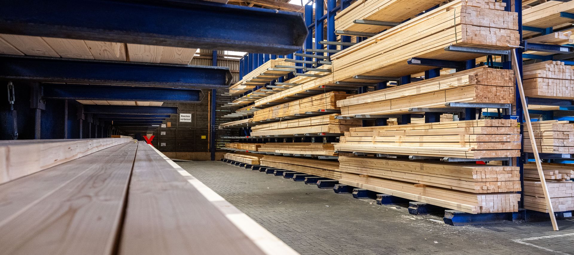 Holzlager von bauXpert Gr. Beilage mit langen Holzbalken in Regalen und Transportwagen im Gang