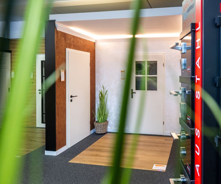 Blume im Vordergrund. Dahinter ein Aufsteller mit Türgriffen von Karcher Design in grau und schwarz. Im Hintergrund die Türenausstellung. Türgriffe und Türenausstellung bauXpert Gr Beilage Vechta Holz Baustoffhandel