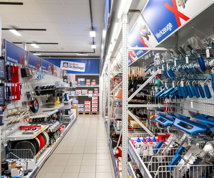 Blick in den Werkzeuggang mit beidseitig bestückten Regalen voller Kellen, Spachtel und Handwerkzeuge im Fachmarkt.