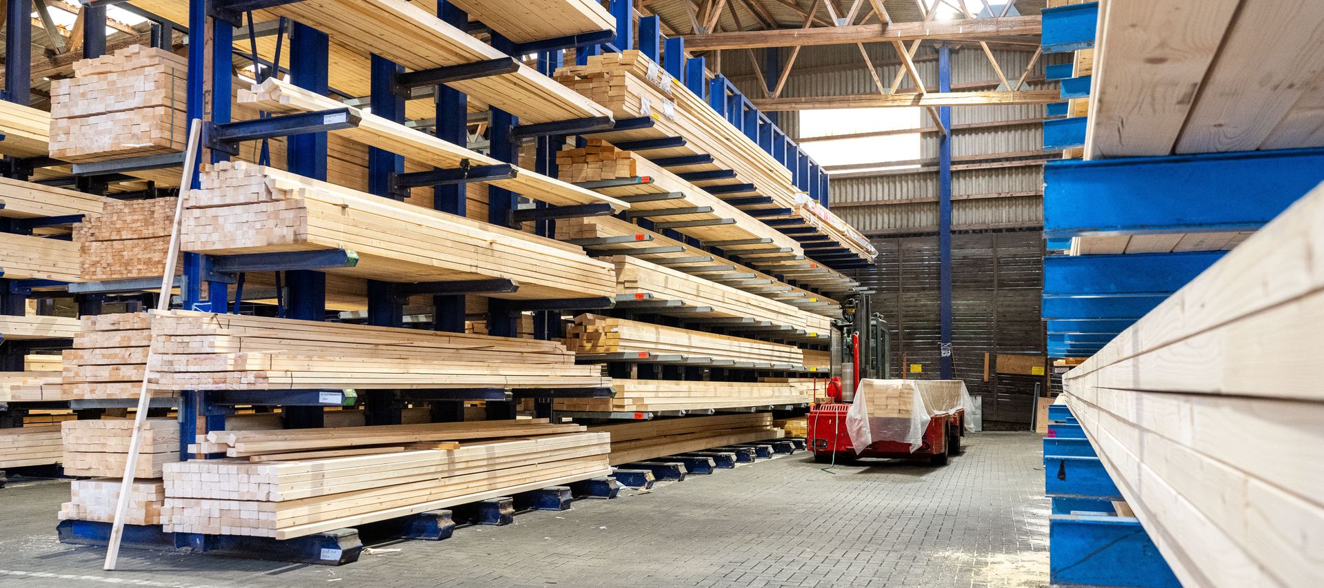 Holzlager von bauXpert Gr. Beilage mit langen Holzbalken in Regalen und Transportwagen im Gang
