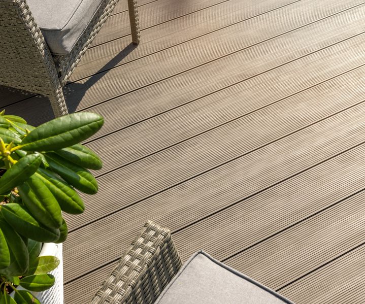 Detailaufnahme von modernen WPC-Terrassendielen mit Rillenstruktur neben Loungemöbeln und Pflanze