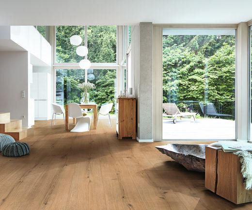 Moderner Wohnraum mit bodentiefen Fenstern und hellem Eichenholzboden, Blick ins Grüne