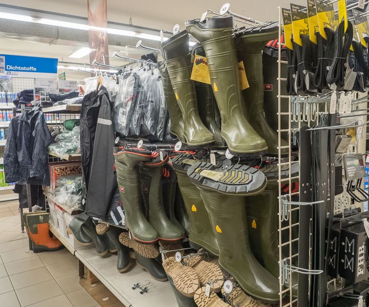 Regal mit Gummistiefeln, Arbeitskleidung und Zubehör für Arbeitsschutz im Innenbereich eines bauXpert Fachmarkts.