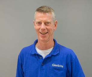 Geschäftsführer von bauXpert steht vor neutralem Hintergrund und lächelt offen in die Kamera. Er trägt Arbeitskleidung mit Namenszug.