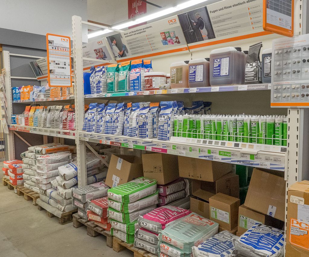 Regalfläche im Fachmarkt mit Bauchemie von PCI, darunter Kleber, Fugenmörtel, Dichtstoffe und Zubehör für Fliesen- und Abdichtungsarbeiten. Die Produkte sind nach Anwendung sortiert.