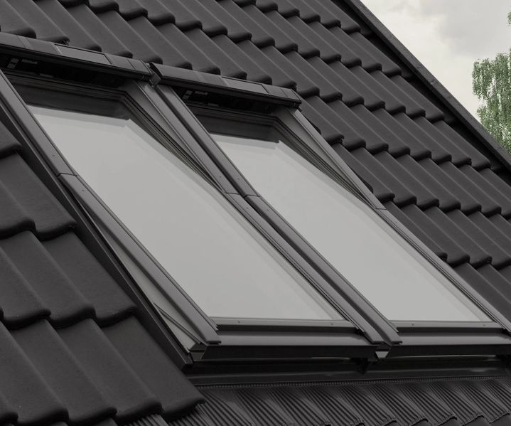 Zwei moderne Dachfenster in einem dunkel gedeckten Ziegeldach, eingebaut nebeneinander auf einer geneigten Dachfläche.