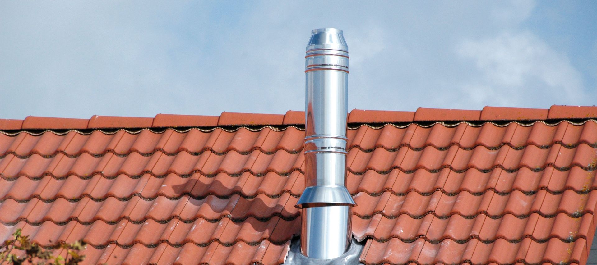 Edelstahlschornstein führt durch ein geneigtes Ziegeldach, sauber eingefasst mit einer Dachabdichtung