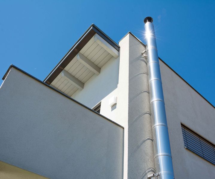 Außenansicht eines Wohnhauses mit montiertem Edelstahlschornstein an der Fassade, aufgenommen aus der Untersicht