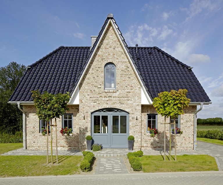 Ein freistehendes Einfamilienhaus mit klassischer Klinkerfassade und dunklem Ziegeldach, symmetrisch angelegtem Eingangsbereich und gepflastertem Weg. Die Fassade wirkt hochwertig und zeitlos.
