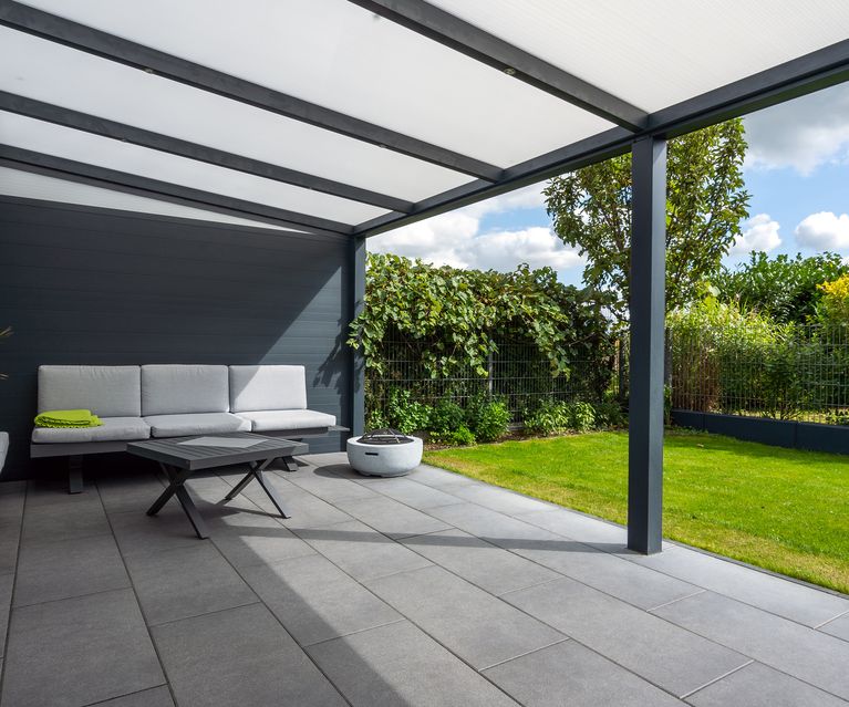 Überdachte Terrasse mit grauen Terrassenplatten, Loungemöbeln und angrenzendem Rasen