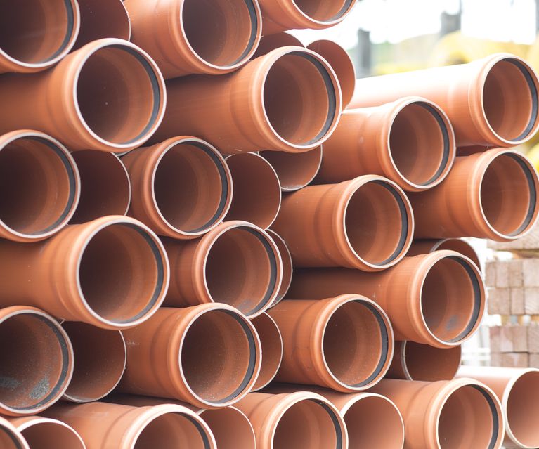 Gestapelte orange KG-Rohre aus Kunststoff für Abwasser- und Entwässerungssysteme auf dem Baustofflager