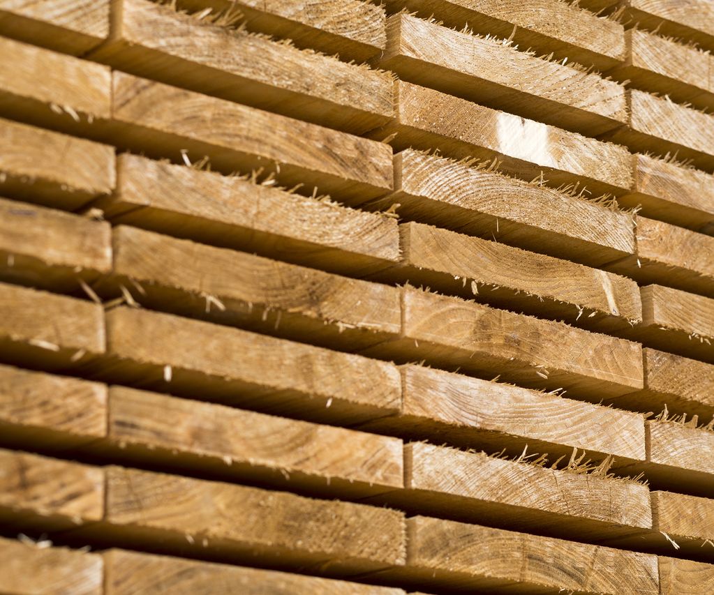 Gestapelte, frisch gesägte Holzbretter mit sichtbarer Maserung und rauer Oberfläche. Die Bretter liegen gleichmäßig übereinander im Lagerbereich.