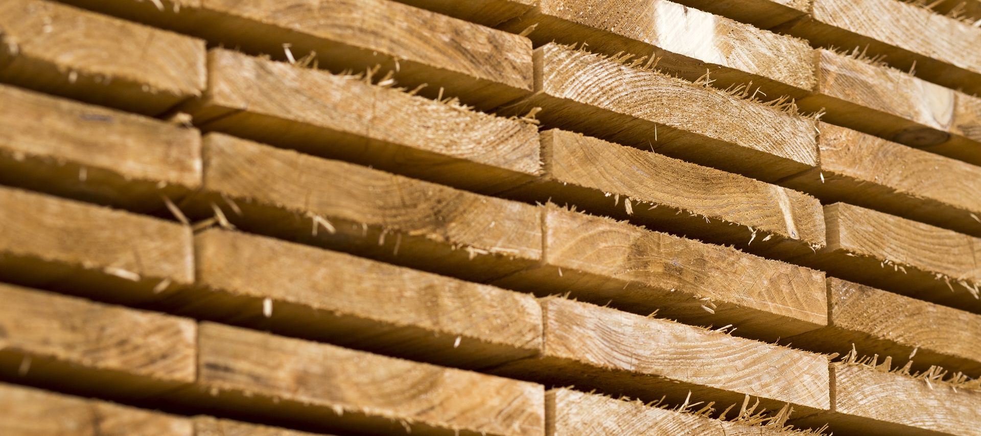 Gestapelte, frisch gesägte Holzbretter mit sichtbarer Maserung und rauer Oberfläche. Die Bretter liegen gleichmäßig übereinander im Lagerbereich.