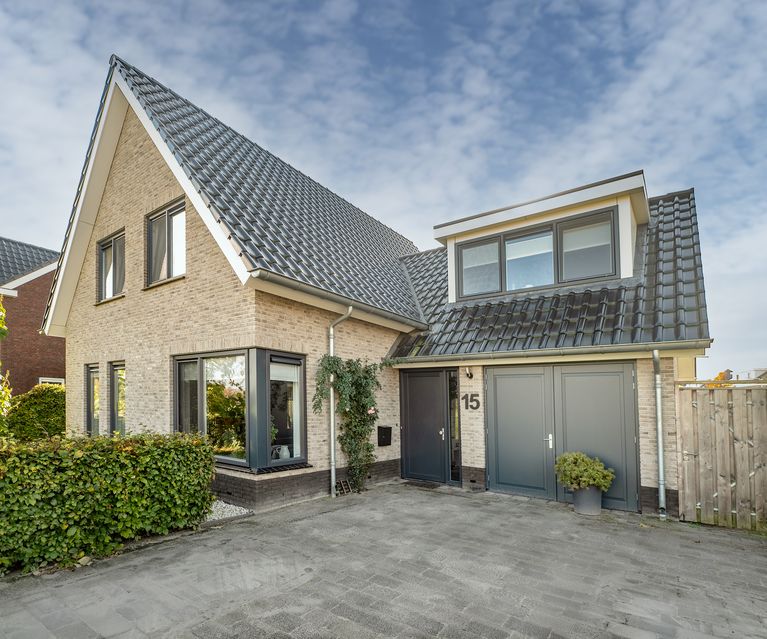 Modernes Einfamilienhaus mit heller Verblenderfassade, anthrazitfarbenem Dach und integrierter Garage. Der Eingangsbereich und die Zufahrt sind klar gestaltet und gepflastert.