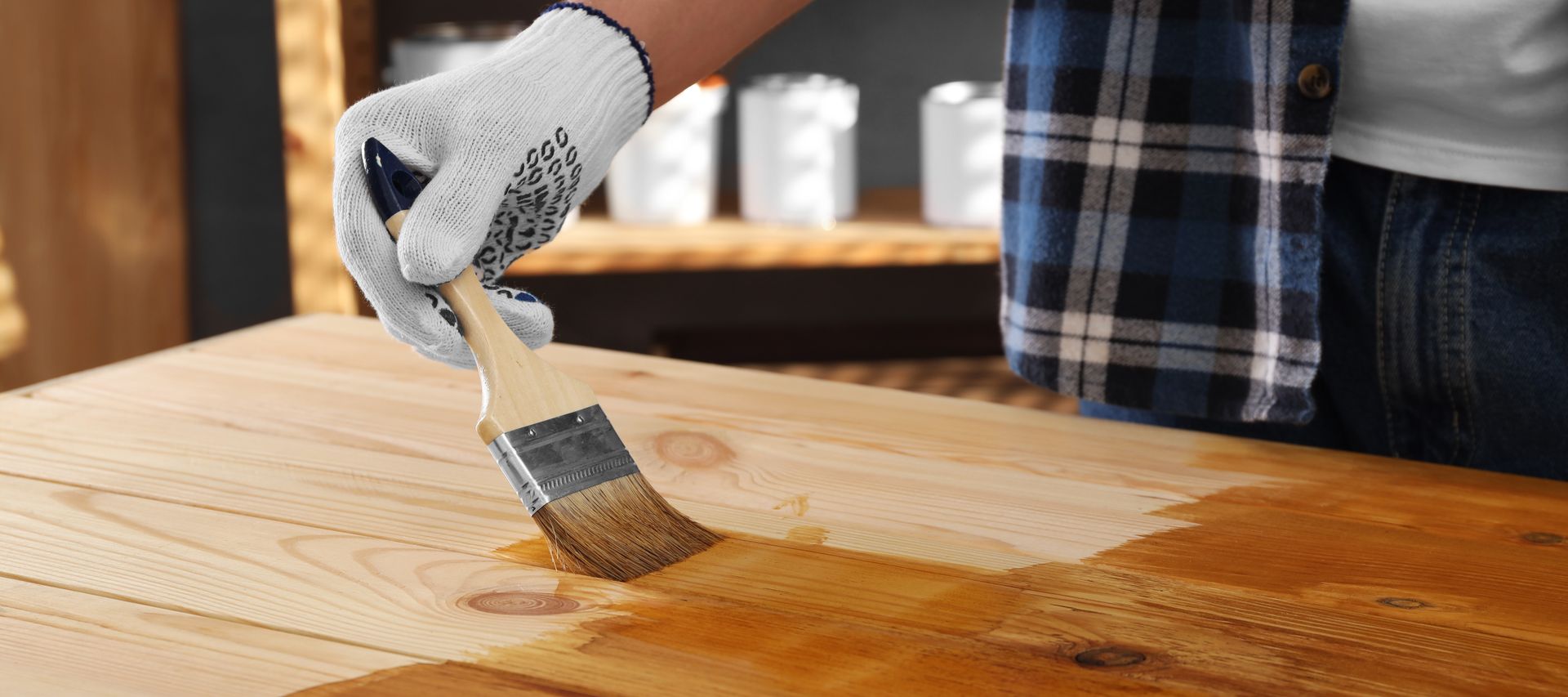 Holzoberfläche wird mit einem Pinsel und Holzschutzlasur gestrichen, Hand mit Arbeitshandschuh trägt gleichmäßig Holzöl auf.