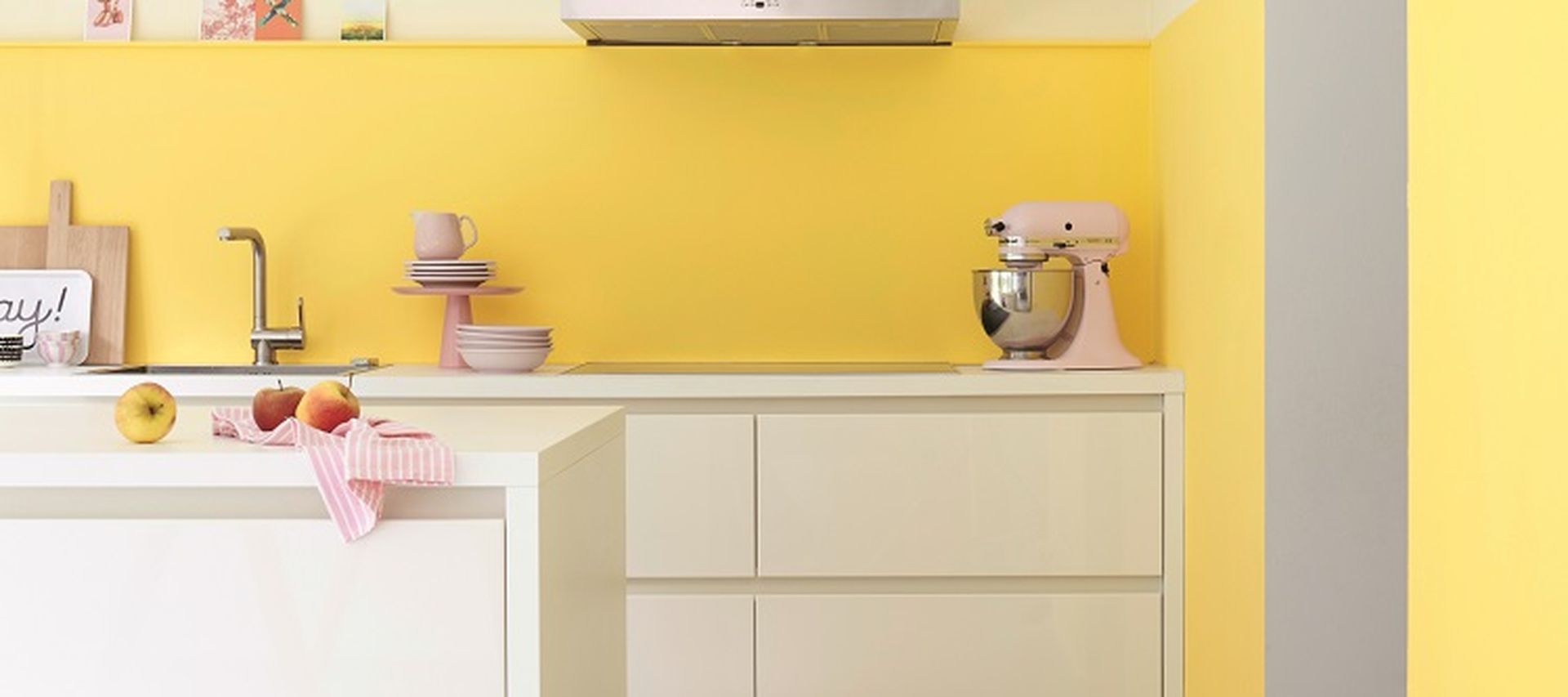 Moderne Küche mit weißer Kücheninsel, gelber Wandgestaltung und klaren Linien in hellem, freundlichem Design.