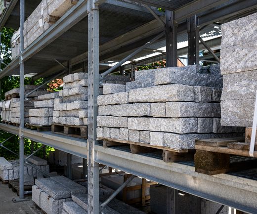 Gestapelte Natursteinplatten und Mauersteine lagern sortiert in einem Außenregal im Baustoffhandel.