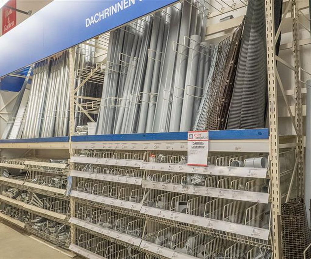 Regalbereich im Fachmarkt mit Dachrinnen, Fallrohren und Zubehör aus Metall. Die Bauteile sind übersichtlich sortiert und in verschiedenen Größen verfügbar.