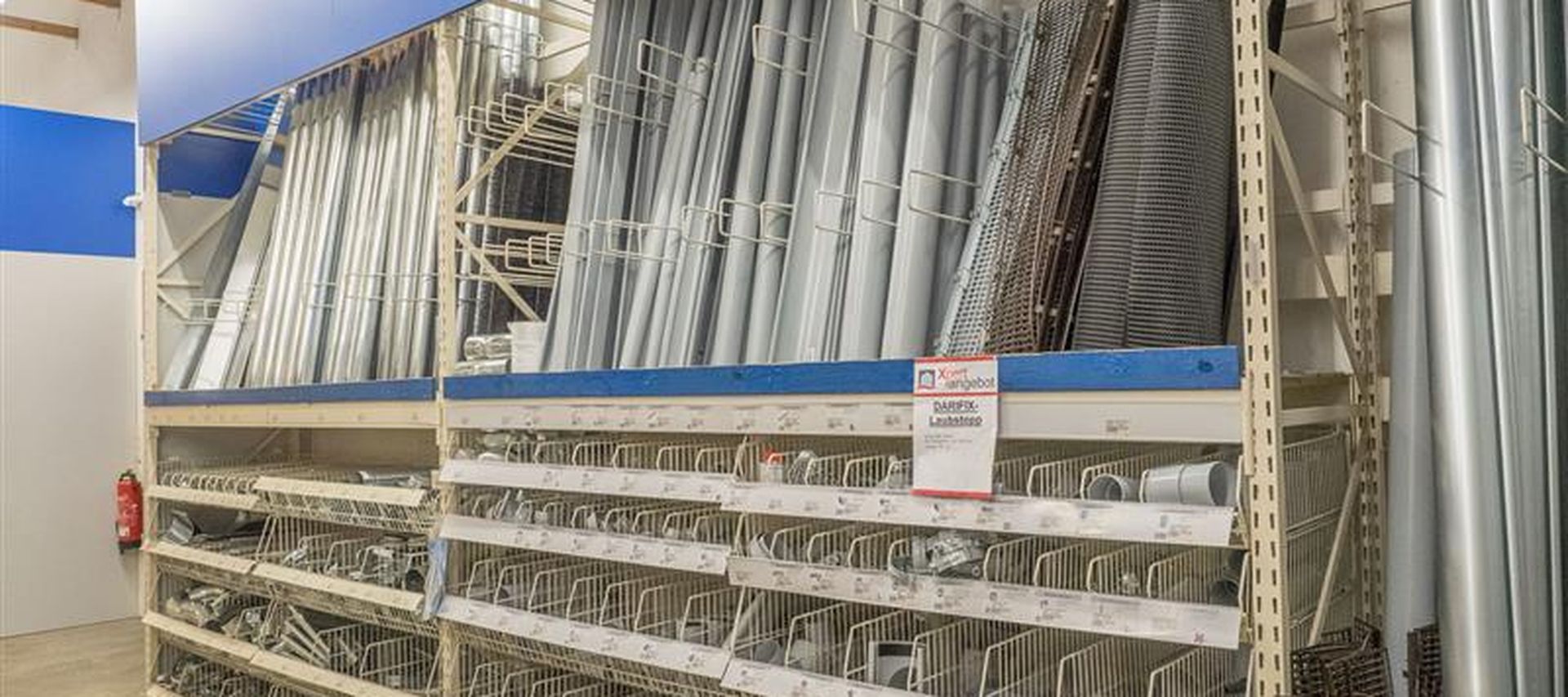 Regalbereich im Fachmarkt mit Dachrinnen, Fallrohren und Zubehör aus Metall. Die Bauteile sind übersichtlich sortiert und in verschiedenen Größen verfügbar.