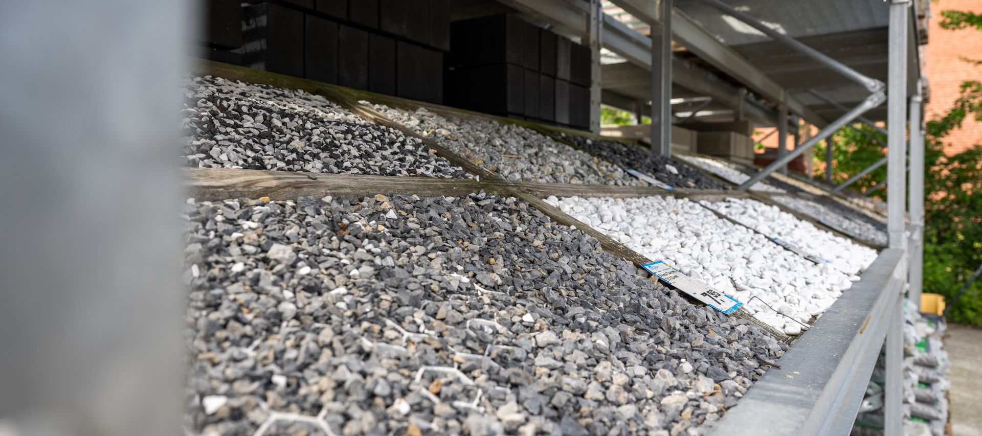 Verschiedene Schüttgüter wie grauer und weißer Zierkies in schrägen Lagerboxen.