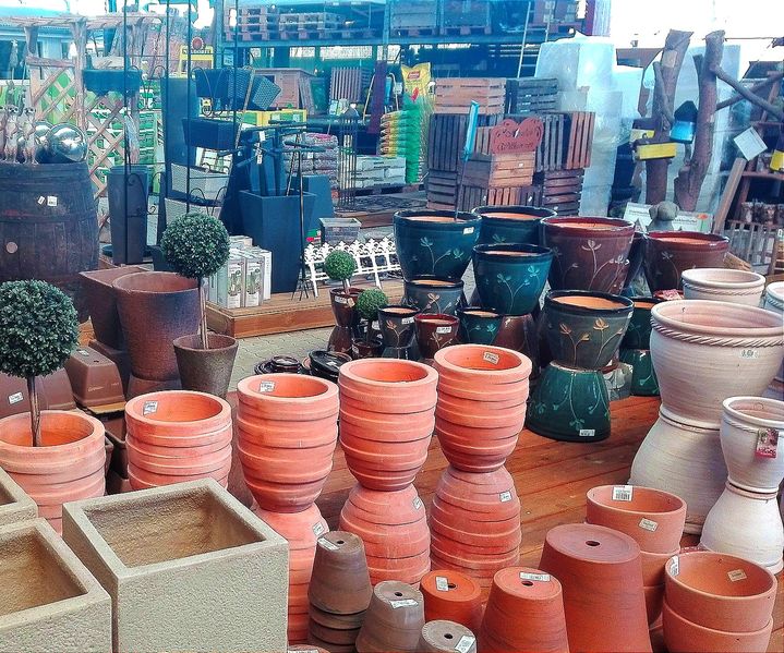 Verschiedene Ton- und Keramiktöpfe in verschiedenen Formen und Größen, ausgestellt in einer Gartenausstellung, mit sichtbaren Pflanzgefäßen und Gartendekor.