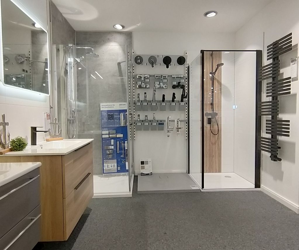 Moderner Badezimmer-Showroom mit Duschkabine aus Glas, Waschtisch aus Holz, Wandarmaturen und eleganter Beleuchtung.