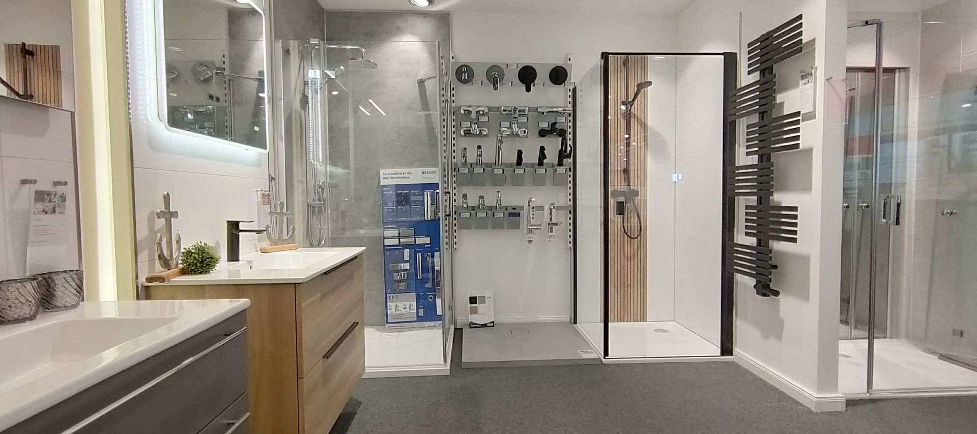 Moderner Badezimmer-Showroom mit Duschkabine aus Glas, Waschtisch aus Holz, Wandarmaturen und eleganter Beleuchtung.