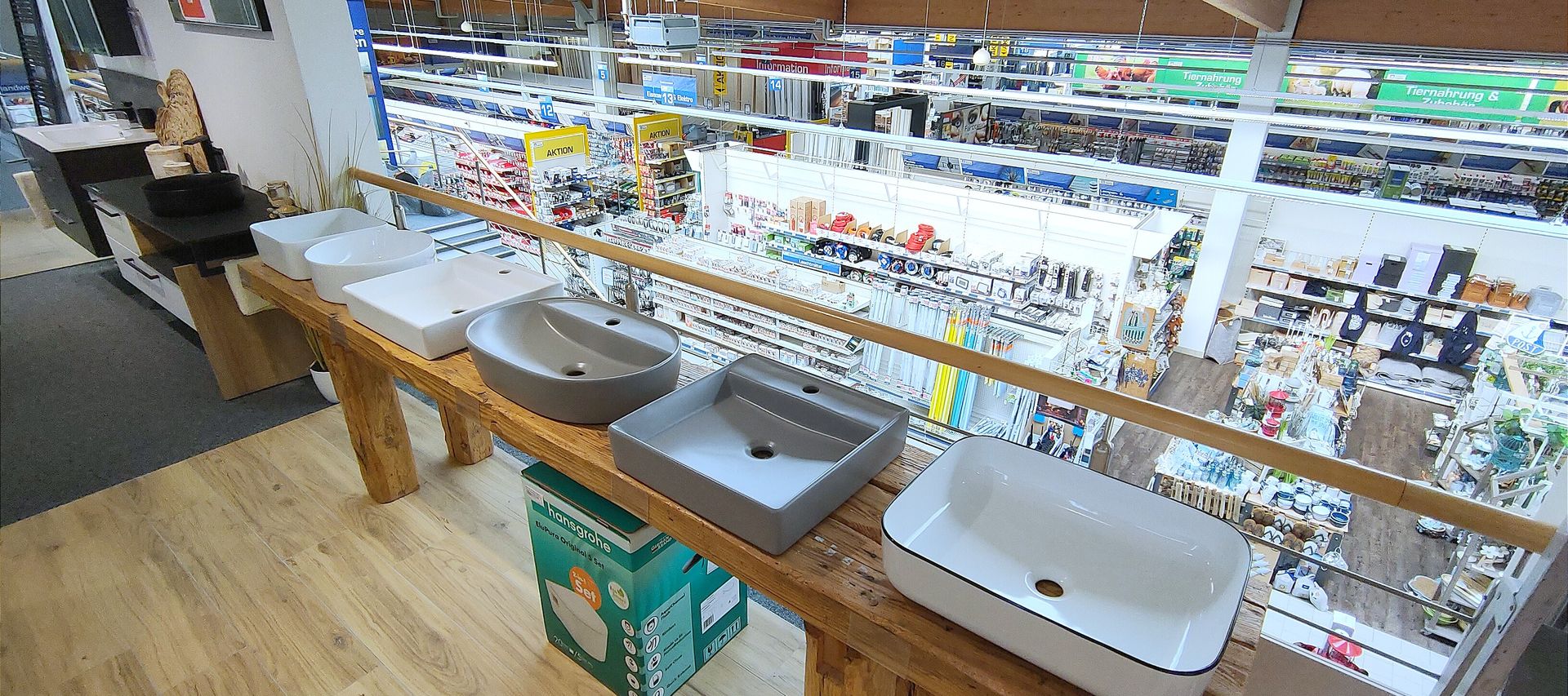 Ausstellung verschiedener Waschbecken auf einer Holztheke im OG mit Blick auf die darunter liegende Ladenetage und Gängen mit Heimwerkerprodukten.