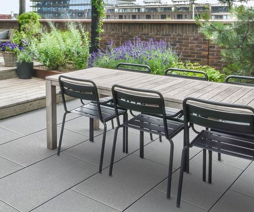 Graue Terrassenplatten auf einer Dachterrasse mit Esstisch, Holzdeck und Pflanzkübeln