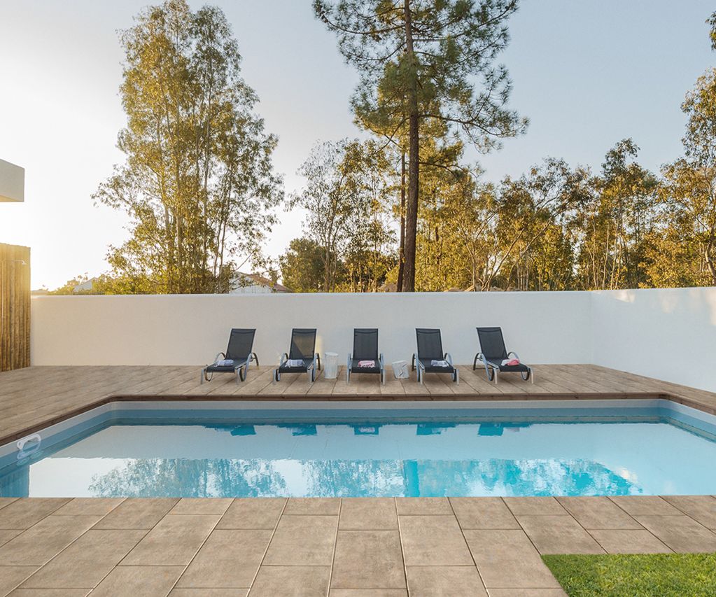 Heller Plattenbelag rund um einen Pool mit Liegestühlen und moderner Hausfassade