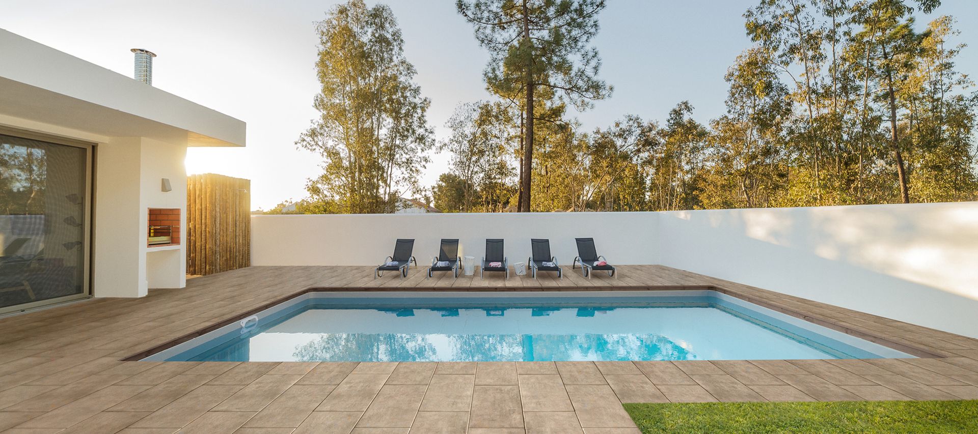 Heller Plattenbelag rund um einen Pool mit Liegestühlen und moderner Hausfassade