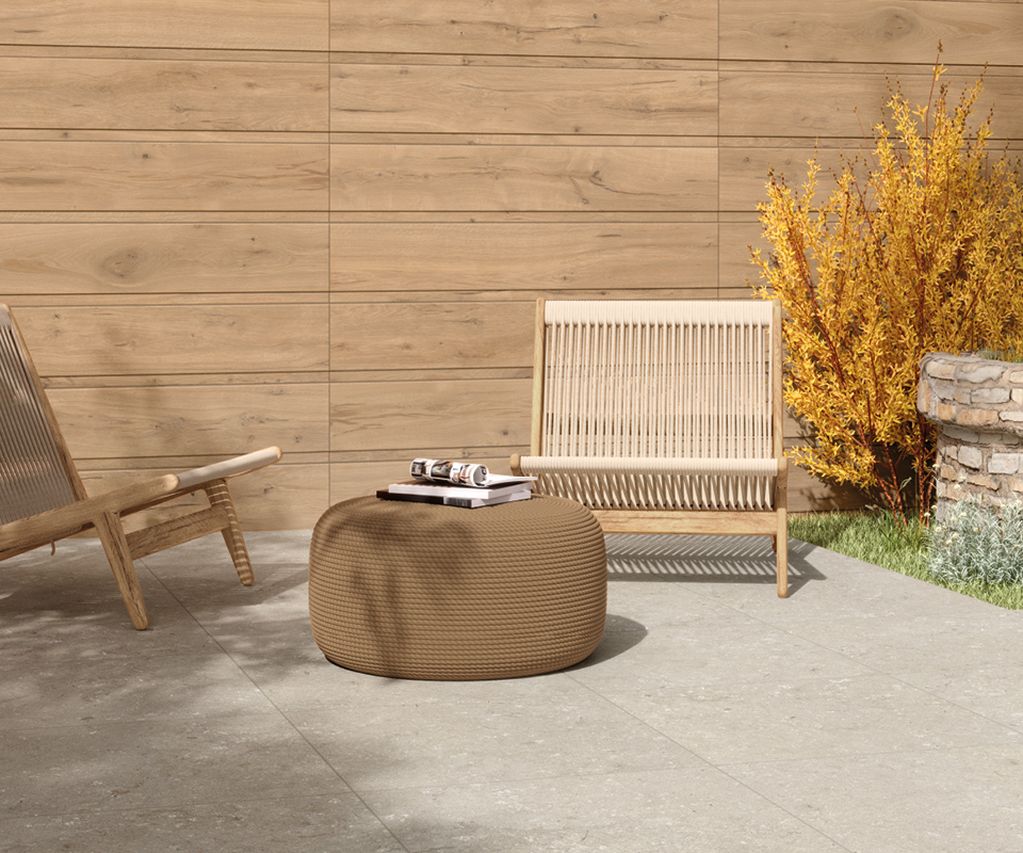 Moderner Terrassenbereich mit großformatigen hellgrauen Keramikterrassenplatten, Sitzmöbeln und bepflanztem Natursteinbeet.