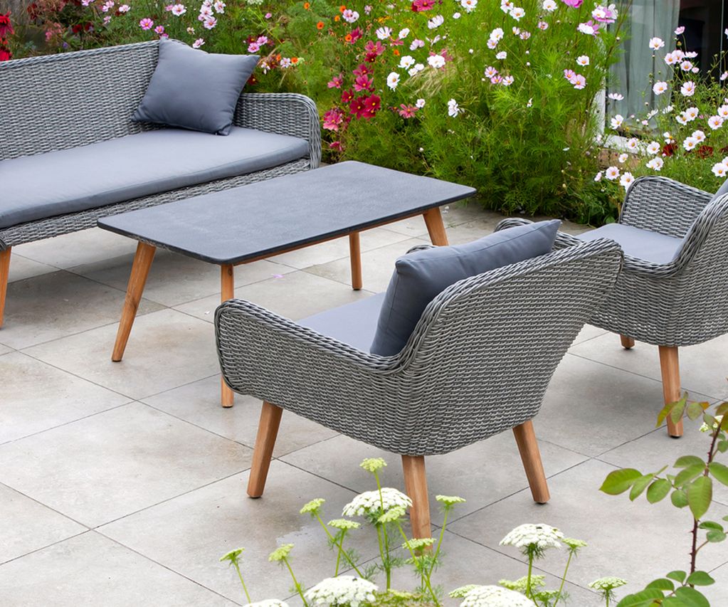 Terrasse mit hellen Keramikterrassenplatten, grauen Gartenmöbeln und blühender Bepflanzung im umliegenden Garten.