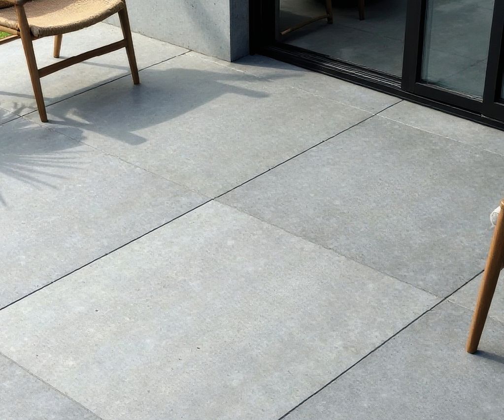 Helle Terrassenplatten vor einer Glasfront mit Holzstühlen und Pflanzkübeln im Außenbereich