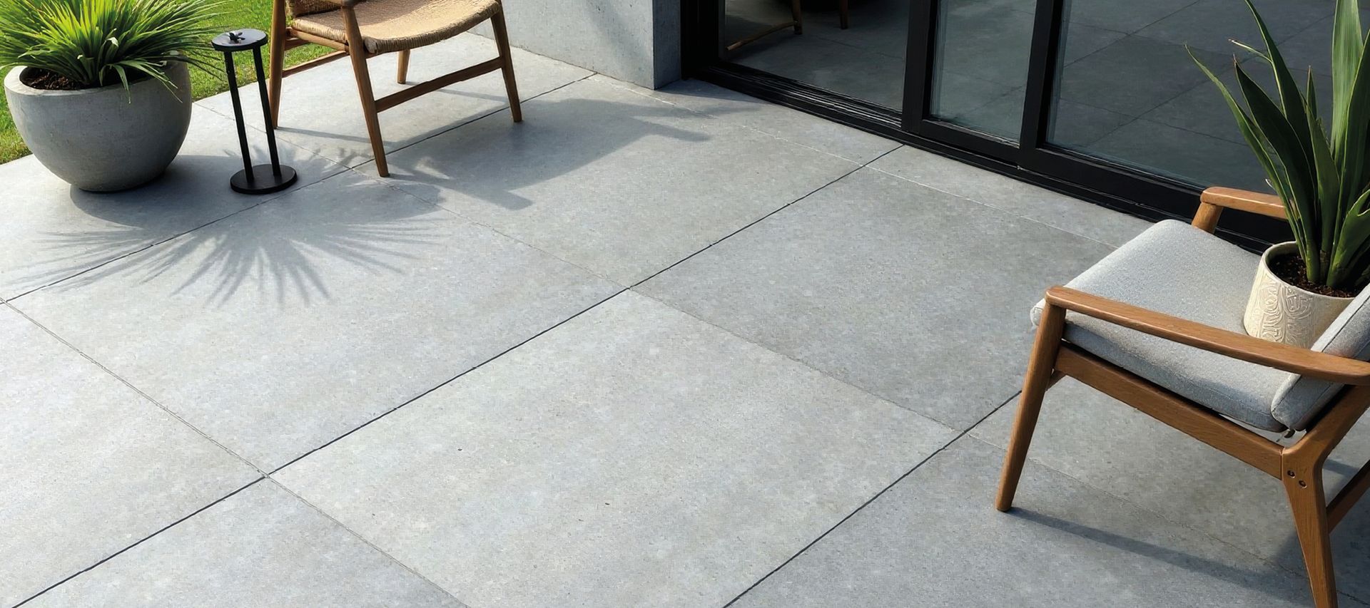 Helle Terrassenplatten vor einer Glasfront mit Holzstühlen und Pflanzkübeln im Außenbereich