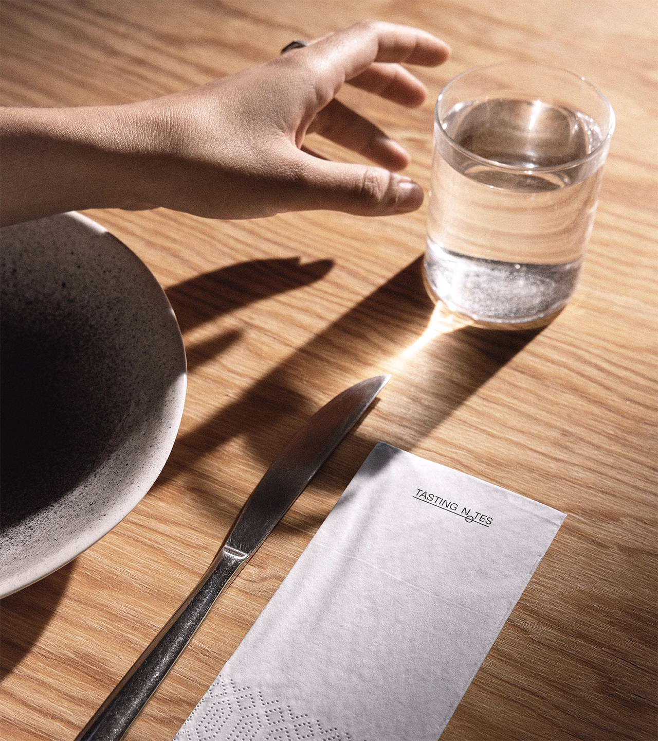 Table setting with a white napkin branded 'Tasting Notes', a glass of water, and cutlery